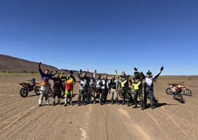 Grupo de motociclistas Pegadas na Aventura a celebrar no deserto de Merzouga, Marrocos, durante uma experiência off-road com motos KTM nas pistas do Sahara.