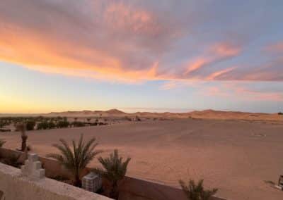 Paisagem do deserto de Merzouga ao pôr do sol, com dunas do Sahara e céu colorido, cenário típico das viagens de moto Pegadas na Aventura em Marrocos