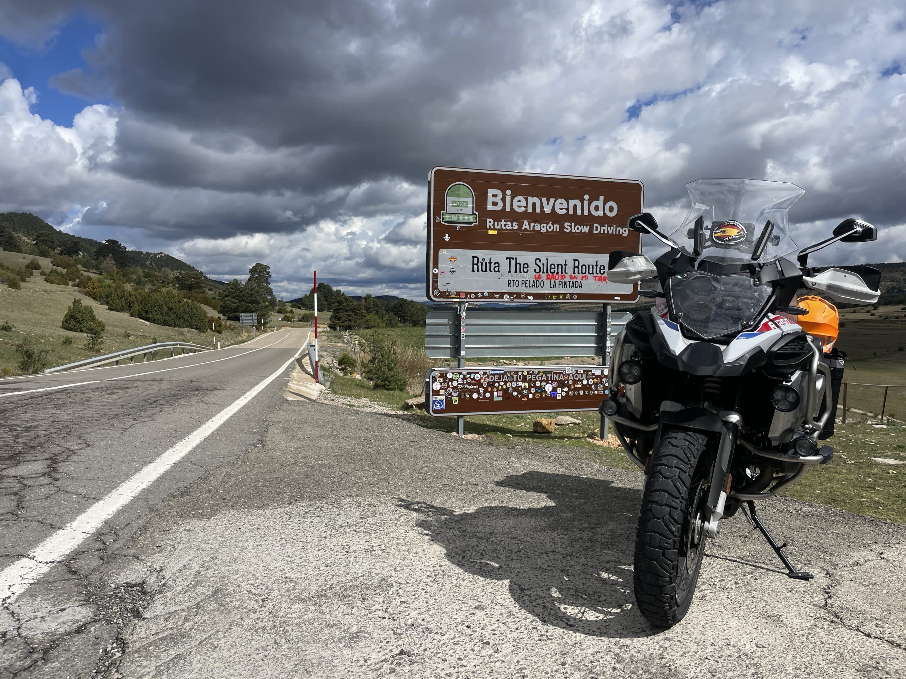Grupo de motos da Pegadas n’Aventura a atravessar um vale no sul de Marrocos, numa estrada panorâmica entre montanhas, durante a viagem Al Maghrib 2026. Paisagens autênticas, cultura berbere e rota ideal para viagens de aventura em moto